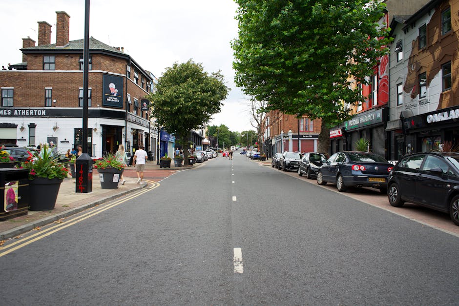 A residential street in West Wickham with a row of Victorian-style terraced houses, featuring white facades, bay windows, and red brick chimneys under a cloudy sky. The pavement runs alongside the hou